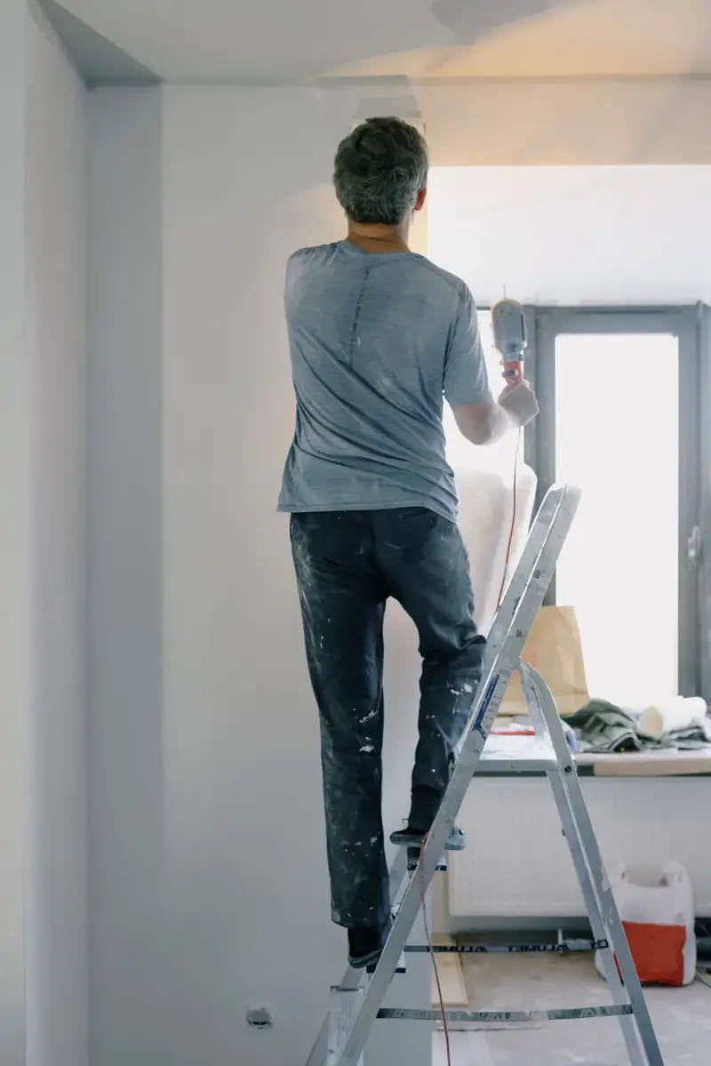 Hausmeister arbeitet auf einer Leiter an einer Wand